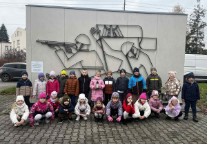 Dzieci stoją przed pomnikiem żołnierzy.