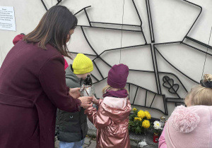 Przedszkolaki stawiają znicz pod pomnikiem żołnierzy.