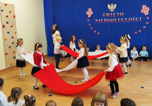 Przedszkolaki tańczą z biało - czerwonymi płótnami.