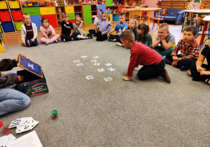 Chłopiec siedzi przed rozłożonymi na dywanie szablonami przedstawiającymi cyfry.