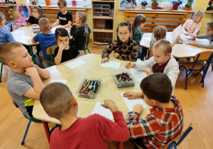 Przedszkolaki siedzą pzrey stolikach i wykonują kartę pracy.