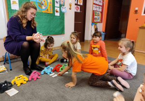 Dzieci na dywanie siedzą przed kolorowymi pluszakami.