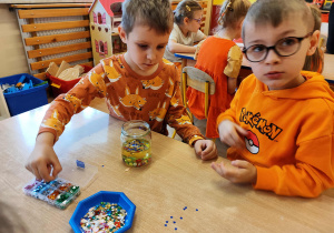 Chłopcy wrzucają do słoika kolorowe cekiny.