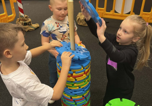 Dzieci układają wieżę z drewnianych klocków.