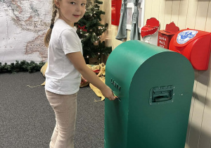 Dziewczynka wrzuca list do skrzynki pocztowej.