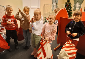 Małe dzieci trzymają worki z prezentami.