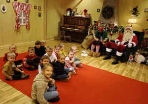 Dzieci siedzą przed Mikołajem.