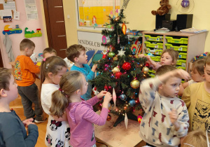 Dzieci dekorują choinkę.