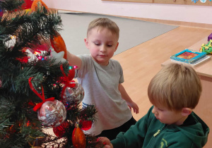 Chłopcy zawieszają bombki na choince.