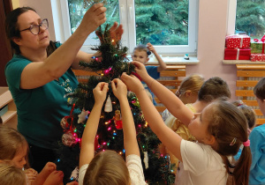 Dzieci zawieszają świąteczne ozdoby na choince.
