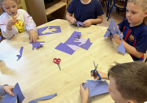 Przedszkolaki siedzą na dywanie i słuchają czytanej książki.