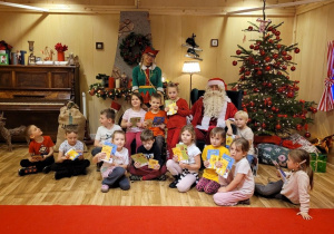 Przedszkolaki siedzą obok Mikołaja i Elfa.