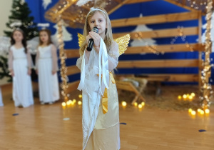 Dziewczynka przebrana za anioła śpiewa kolęde.