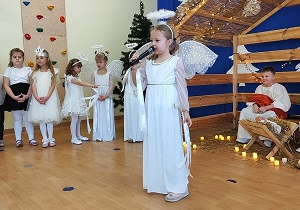 Dziewczynka przebrana za anioła trzyma w ręku mikrofon.