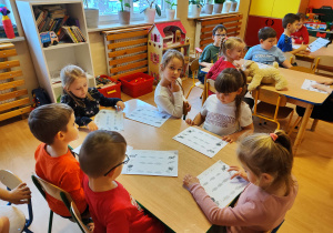 Dzieci przy stoliku wykonują kartę pracy.