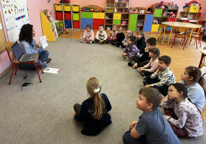 Małe dzieci siedzą w kręgu na dywanie.