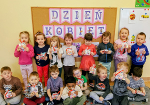 Dzieci trzymają prezenty na tle napisu Dzień Kobiet.