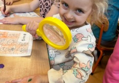 Dziewczynka trzyma lupę w ręku.